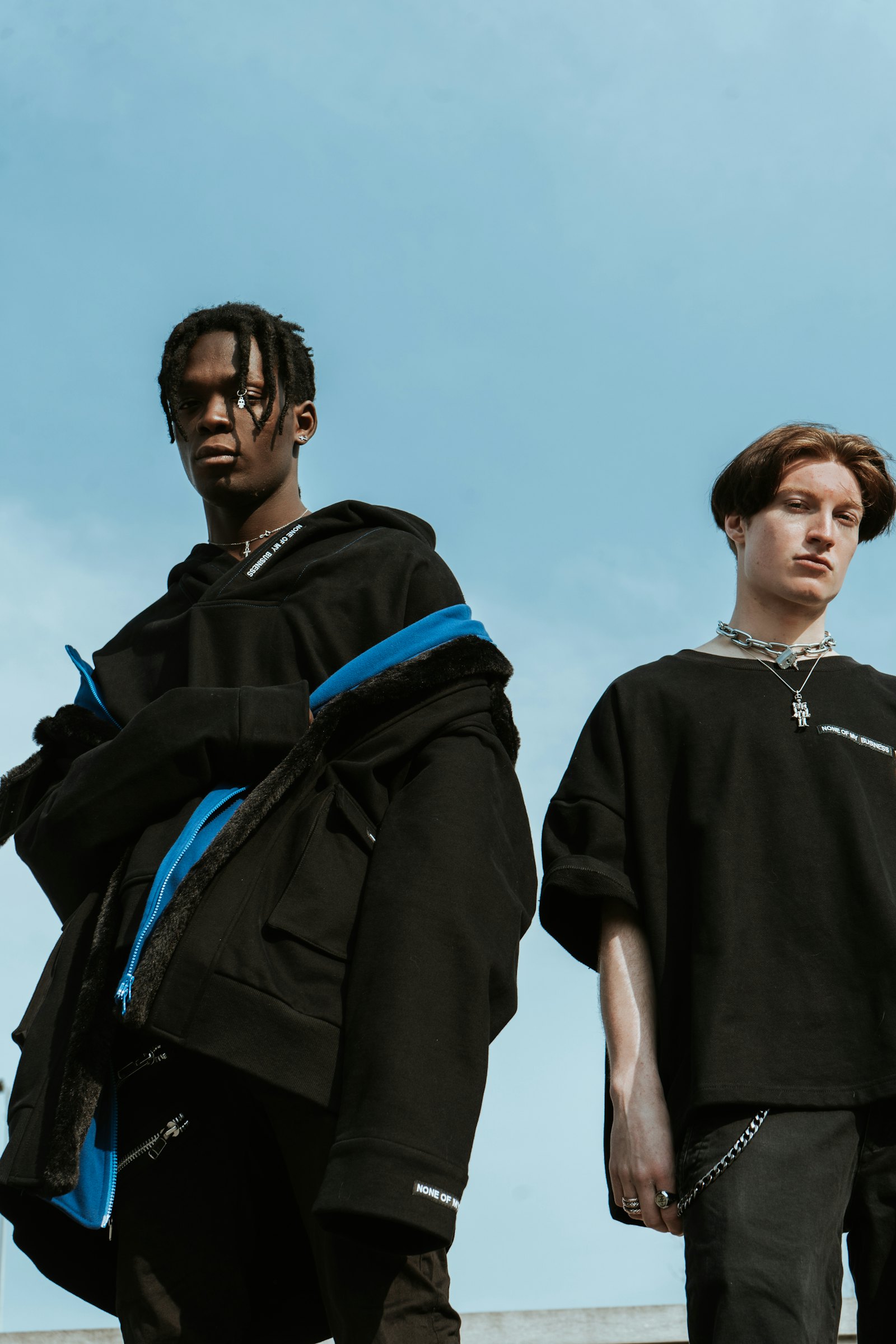 Twee jongens in zwarte OUTRUN-streetwear tegen een blauwe lucht